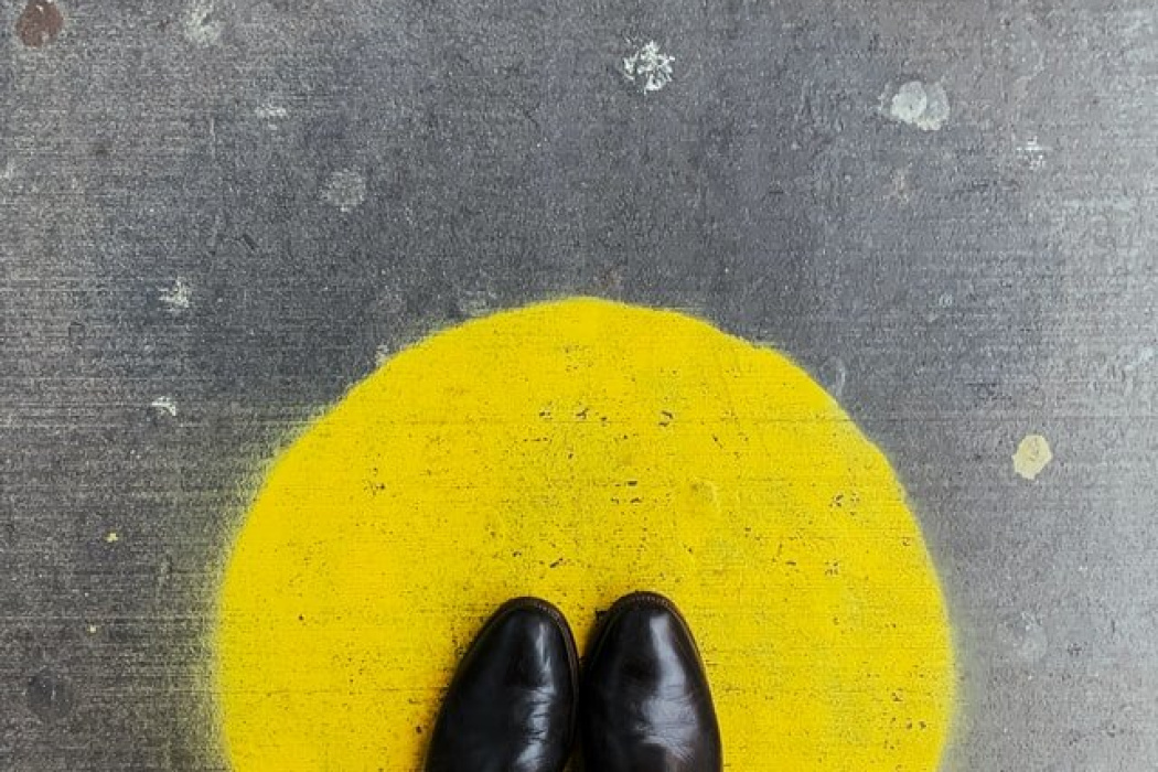 Person standing on a yellow circle painted on the ground, wearing black shoes, symbolizing a moment of pause or focus.